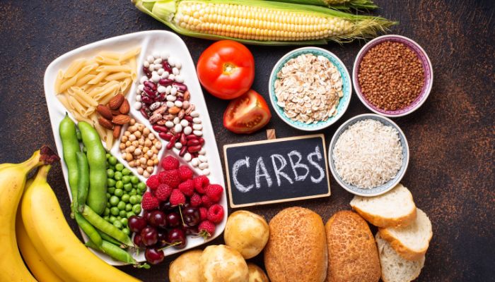 Imagem de cima de uma mesa repleta de produtos ricos em carboidratos como pães, grãos, vegetais e cereais.