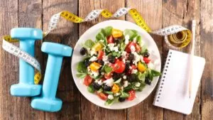 Nutrição para Corredores: imagem de uma prato natural no centro de uma mesa e, ao lado, alteres de academia e uma fita métrica.