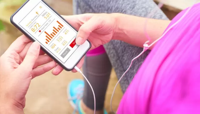 treinamento_de_corrida_online_tecnologia Imagem de um celular trazendo dados estatísticos na tela. Corredores segura o aparelho que está conectado a um fone de ouvido.