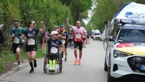 Imagem de corredores em uma estrada, conduzem um cadeirantes e acenam para o Catch Car.