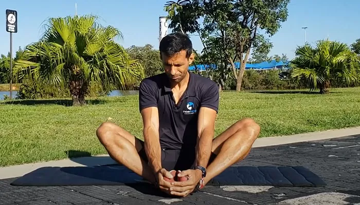 alongamento_para_corrida_exercicio_borboleta Atleta sentado no chão com pernas unidas em forma de borboleta. Ele segura os pés também unidos.