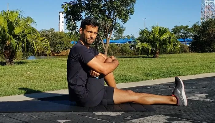 alongamento_para_corrida_exercico_abraca_perna Alongamento apra corrida: atleta está sentado enquanto abraça uma das pernas.